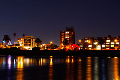 Illuminated buildings by river against sky at night