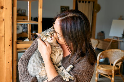 Middle-aged woman hugging cute tabby cat in indoor scene. human-animal relationships. funny home pet