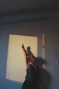 Woman with braided hair and hand raised standing against wall