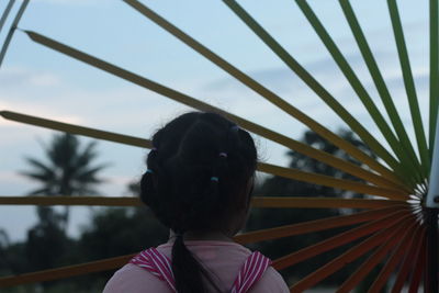 Rear view of girl standing by wheel against sky during sunset