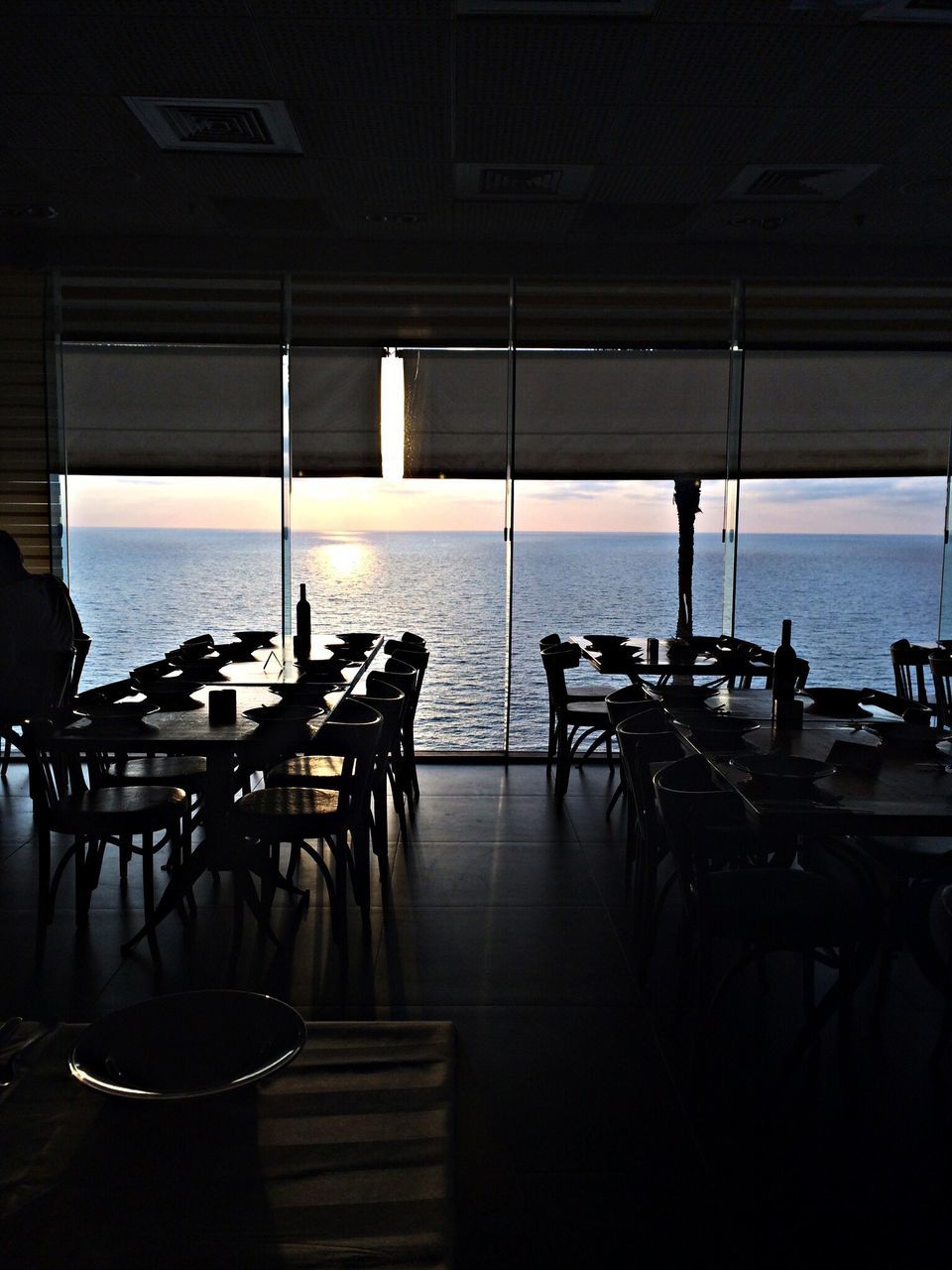 sea, table, chair, water, indoors, restaurant, horizon over water, empty, absence, place setting, sunlight, window, sky, seat, built structure, cafe, no people, day, tourist resort, in a row