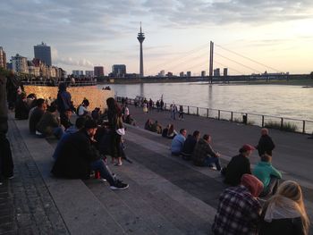 People sitting on bridge over river in city against sky