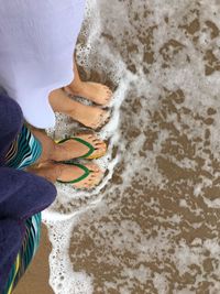 Low section of couple standing on shore at beach