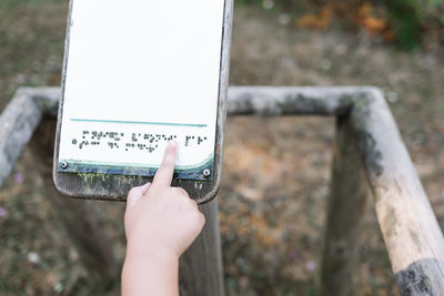 From above anonymous kid touching and reading braille on blank signboard while visiting park on weekend day