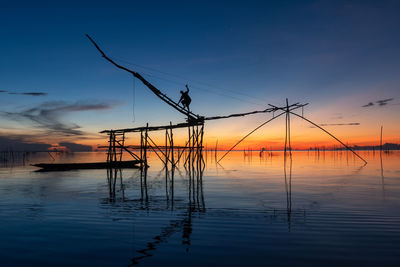 Silhouette wooden posts in sea against sky during sunset