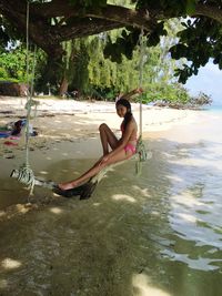 Young woman sitting by lake against trees