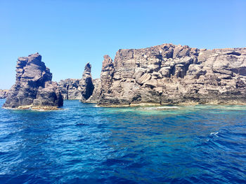 Rocks by sea against clear blue sky