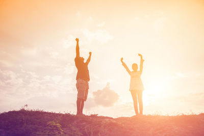 Low angle view of friends standing on land against sky during sunset