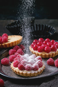 Close-up of powdered sugar falling on dessert with raspberries