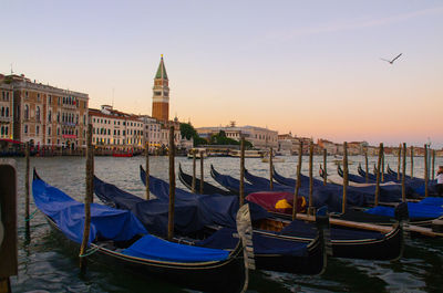 Boats moored at dock against sky in city at dusk