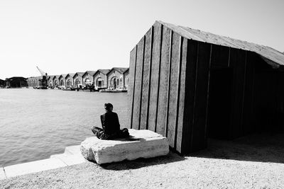 Man sitting on built structure against clear sky