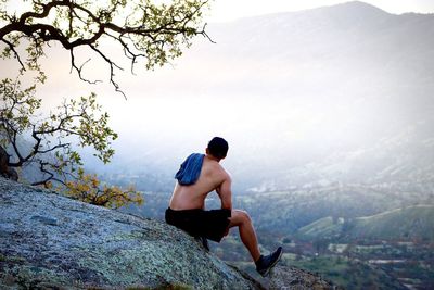 Rear view of shirtless man looking at mountain against sky