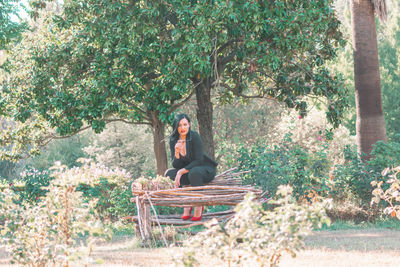 Woman sitting on seat against trees
