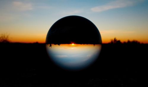 Close-up of silhouette crystal ball on land against sky during sunset