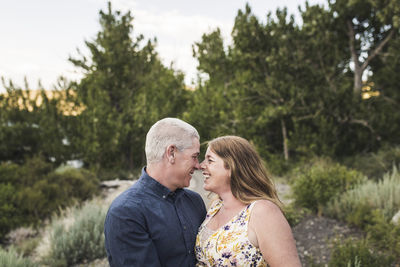 Happy romantic couple rubbing noses while standing against trees in forest