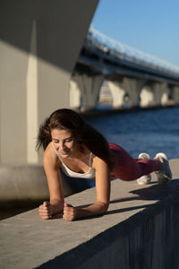 Full length of woman exercising against bridge and sky