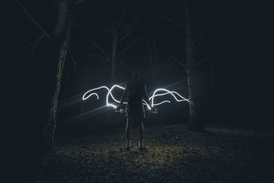 Rear view of person with light painting standing on field at night