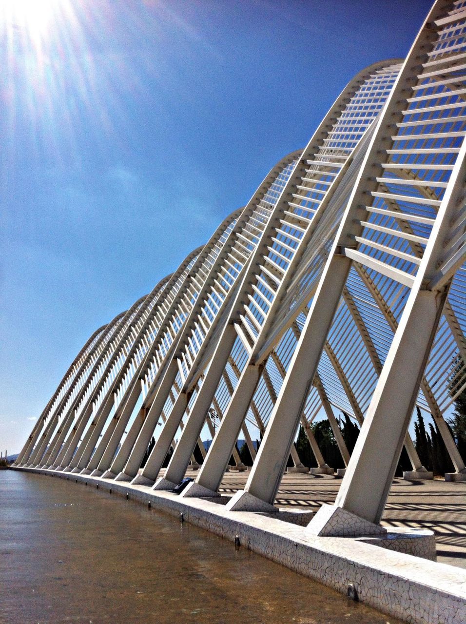 architecture, built structure, low angle view, sunlight, building exterior, sky, blue, sunbeam, sunny, modern, railing, sun, city, lens flare, tall - high, day, outdoors, clear sky, no people, bridge - man made structure