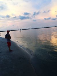 Rear view of man standing on beach against sky during sunset