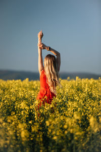 Rear view of woman standing amidst yellow flowering plants on field against sky