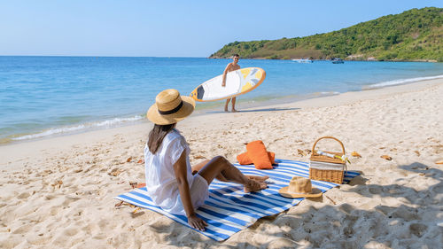 Rear view of woman sitting on beach against sky