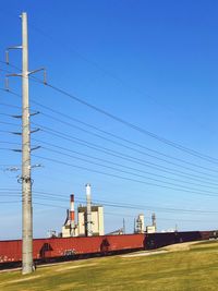 Electricity pylon on field against clear blue sky