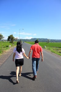 Rear view of couple walking on road against sky