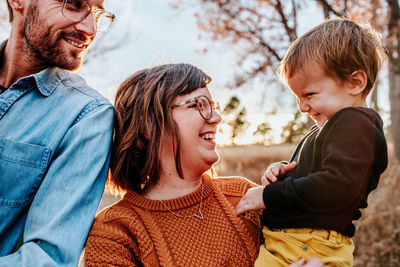 Parents smiling and laughing at young child on a fall evening