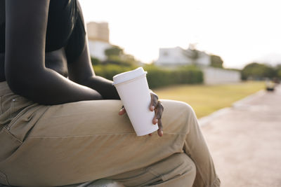 Woman holding coffee cup while sitting on bench at public park