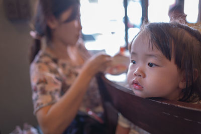 Thoughtful baby girl sitting on chair with mother in restaurant