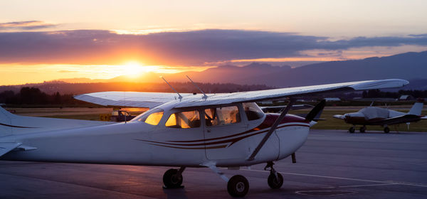 Airplane on runway against sky during sunset