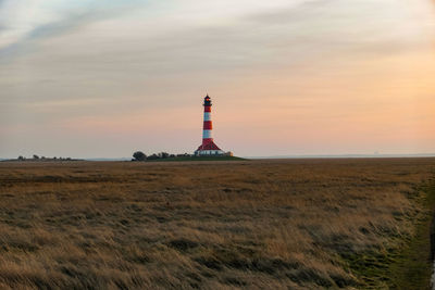 Lighthouse on field against sky at sunset