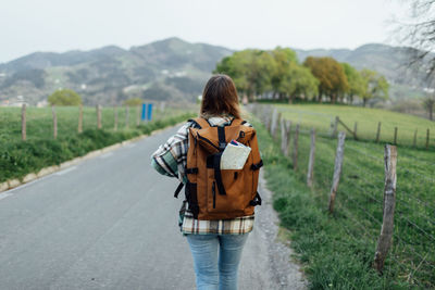 Rear view of woman walking on road amidst field