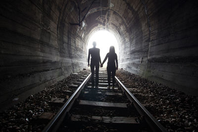 Rear view of silhouette people walking on railroad track