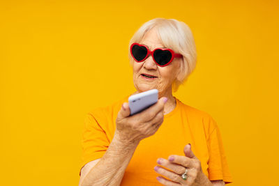 Portrait of senior woman showing mobile phone against colored background
