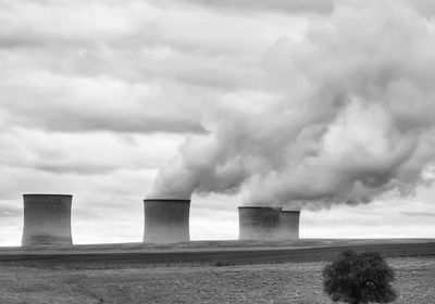 Smoke emitting from factory against cloudy sky