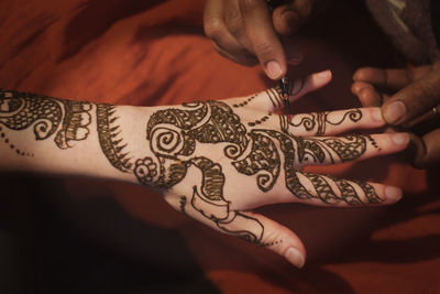 Midsection of woman applying henna on cropped hand