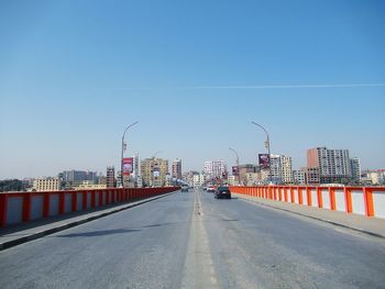 Road by buildings against clear blue sky