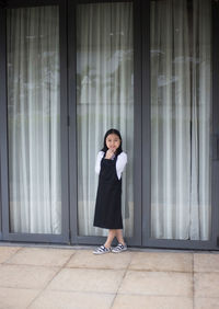 Portrait of cute girl standing on footpath against doorway