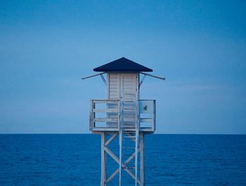 Lifeguard hut by sea against clear blue sky
