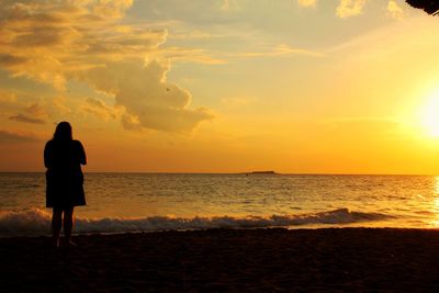 Rear view of silhouette woman standing on beach during sunset