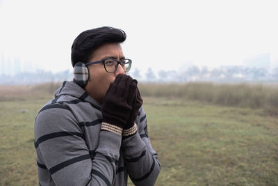 Young man wearing sunglasses standing on field against sky during winter