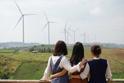 Rear view of friends with arm around standing against landscape