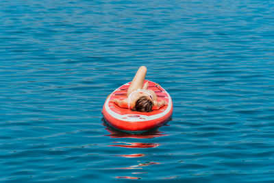 Low angle of a woman relaxing in the sun on a standup paddle board in beautiful blue water.