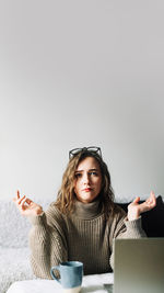 Portrait of young woman using mobile phone while sitting against white background