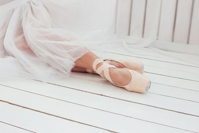 Low section of woman wearing ballet shoes while sitting on wooden floor