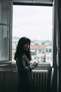 Side view of young woman looking through window