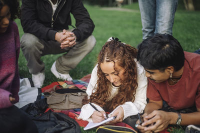 Teenage girl writing in book while lying down next to male friend at park