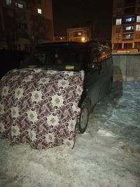 Car on snow covered street in city at night