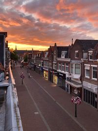 A residential street with a few people and shops with a cloudy orange sky during sunset